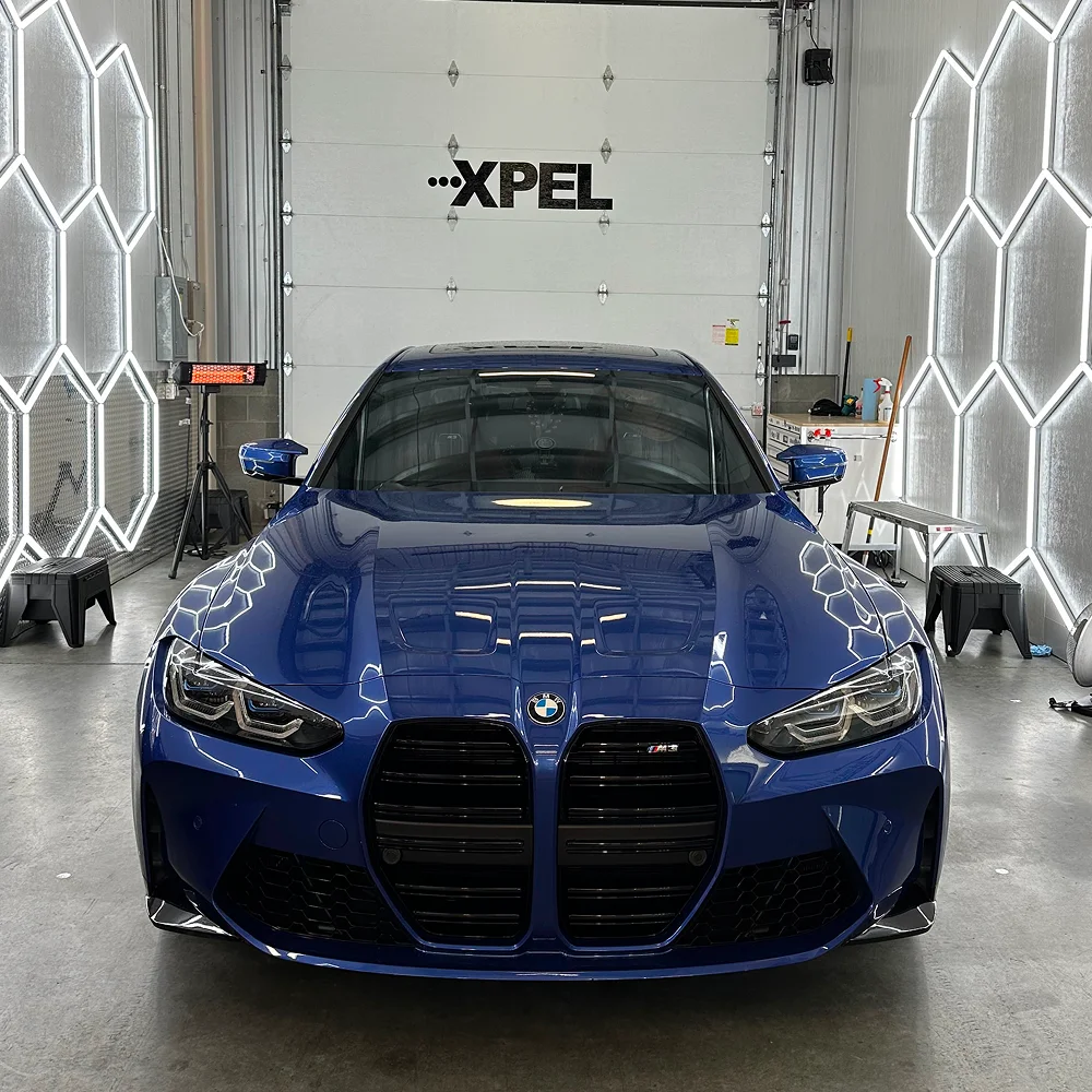 Blue BMW M4 with glossy ceramic coating reflecting detailing lights inside XPEL-certified studio