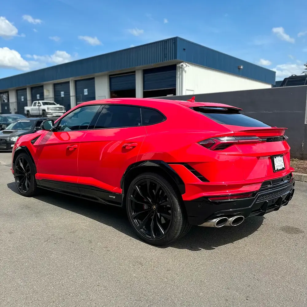 Red Lamborghini Urus with dark tinted windows and black wheels parked outside detailing shop