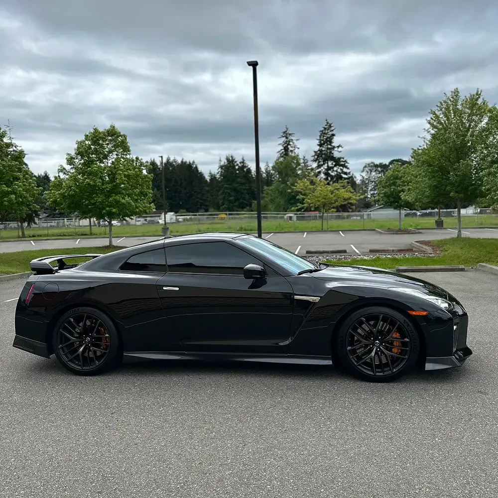 Black Nissan GT-R with dark window tint and black wheels parked in empty lot under overcast sky