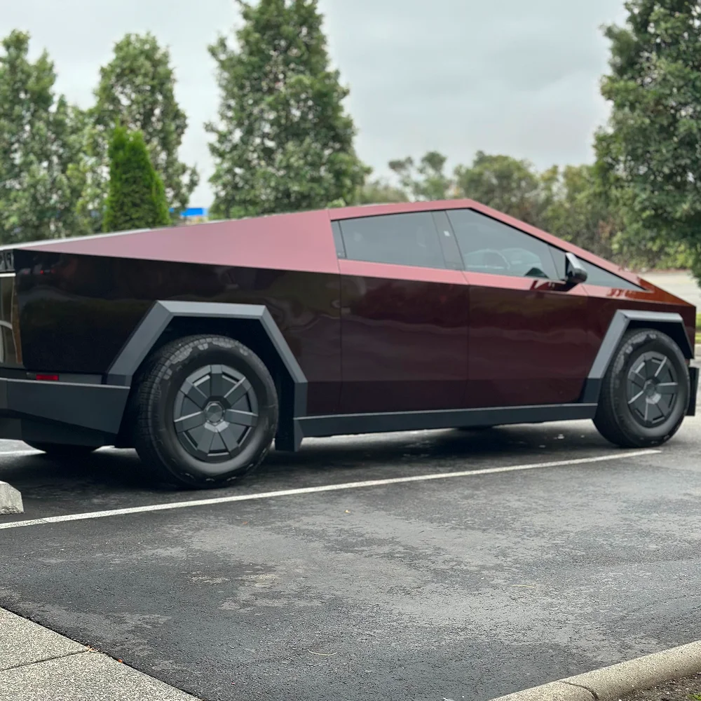 Dark red Tesla Cybertruck with tinted windows and matte finish parked on wet pavement