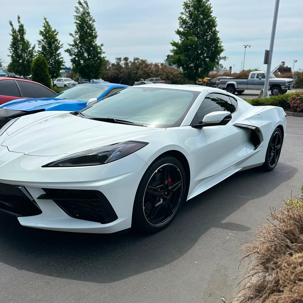 White Chevrolet Corvette C8 with dark window tint and black wheels parked on asphalt near other sports cars