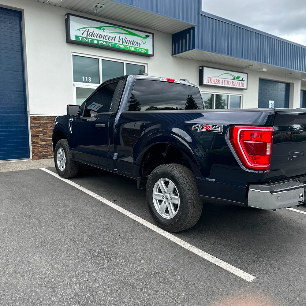 Black Ford 4x4 pickup with dark window tint parked in front of Advanced Window Tint & Paint Protection shop