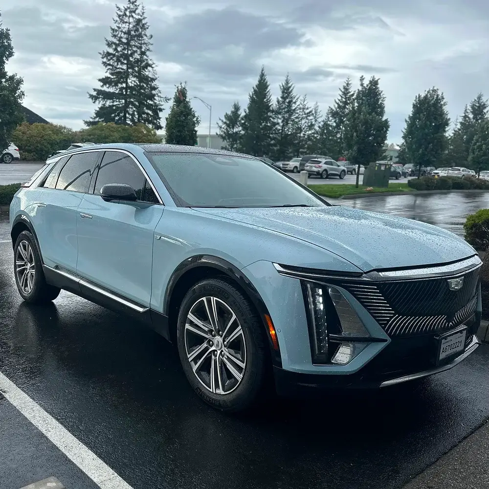 Light blue Cadillac Lyriq SUV with fresh window tint parked in wet parking lot on rainy day