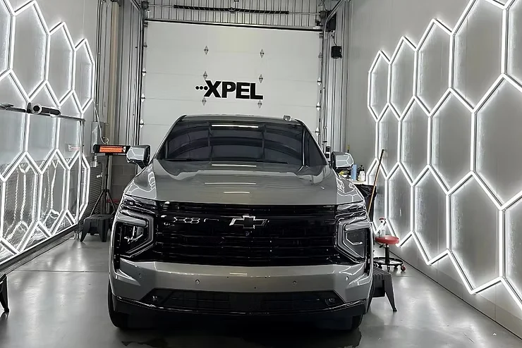 Front view of a gray Chevy truck inside a detailing studio with XPEL branding, showcasing a freshly installed self-healing paint protection film