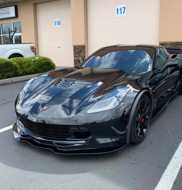 Black sports car with ceramic coating reflecting the sky, parked outside detailing shop