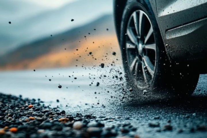 Close-up of a car tire kicking up loose gravel and debris while driving on a rocky road, visually emphasizing how paint protection film helps prevent damage from road hazards like flying stones.
