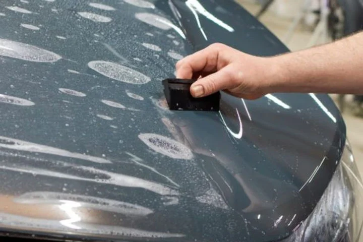A person using a squeegee to apply clear paint protection film onto a wet car hood, demonstrating how PPF provides invisible protection while preserving the vehicle’s original appearance.