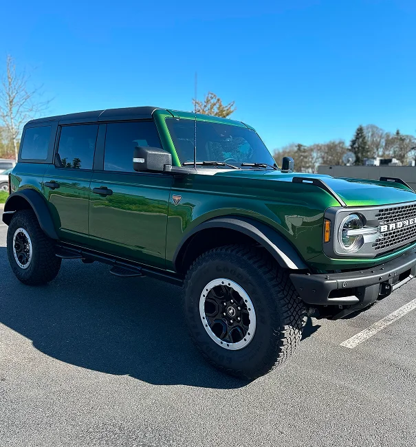 Green Ford Bronco with dark ceramic window tint and black trim parked in sunlight on pavement