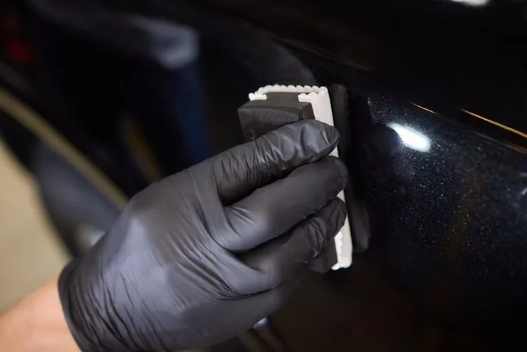 Gloved hand applying ceramic coating to a glossy black car panel using an applicator pad