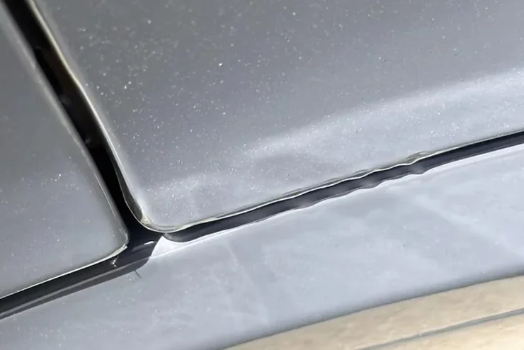 Close-up of paint protection film lifting and wrinkling near the edge of a car panel, showing early signs of poor maintenance or moisture damage