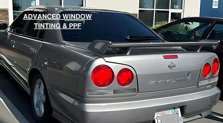 Silver Nissan Skyline with dark tinted windows parked outside a building, showcasing advanced automotive window tinting and paint protection film