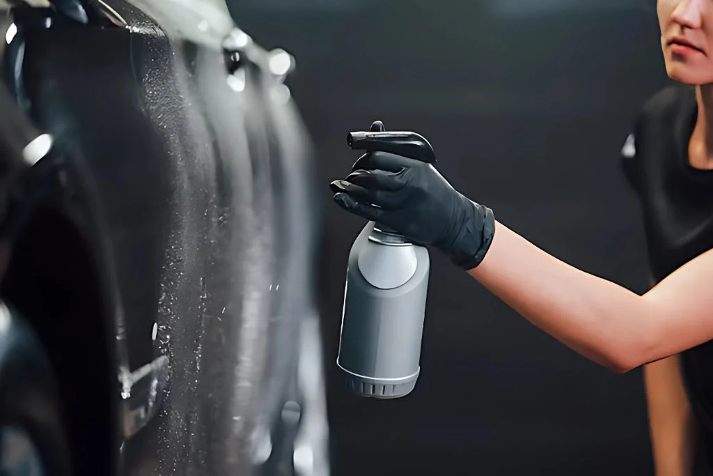 Person in black gloves applying detailing spray to a black car during Paint Protection Film (PPF) maintenance