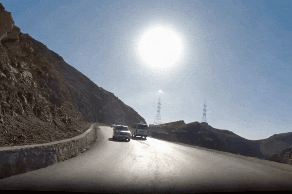 Car driving on a sunlit mountain road with harsh sunlight and rocky terrain, illustrating environmental exposure that can damage vinyl wraps