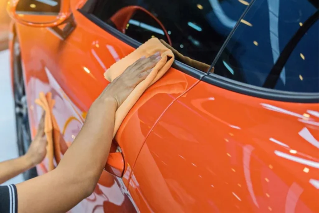 Person using a soft orange microfiber cloth to clean the door of a glossy orange vinyl-wrapped car