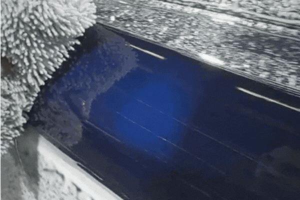 Close-up of a heavily soiled vinyl-wrapped vehicle surface during a car wash, highlighting the buildup of grime and the importance of regular cleaning.