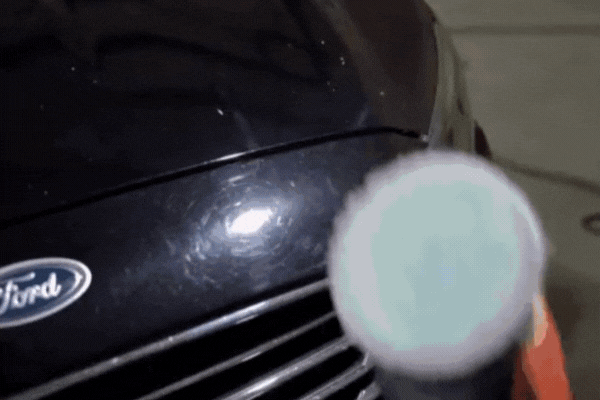 Detailing technician using a dual-action polisher on the hood of a black Ford vehicle, beginning the ceramic coating removal process to restore paint clarity and correct surface imperfections.