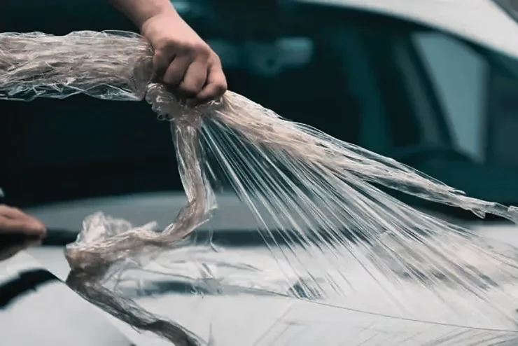 Close-up of a person peeling or applying paint protection film on a car in cold weather, illustrating potential adhesion issues if not installed properly.