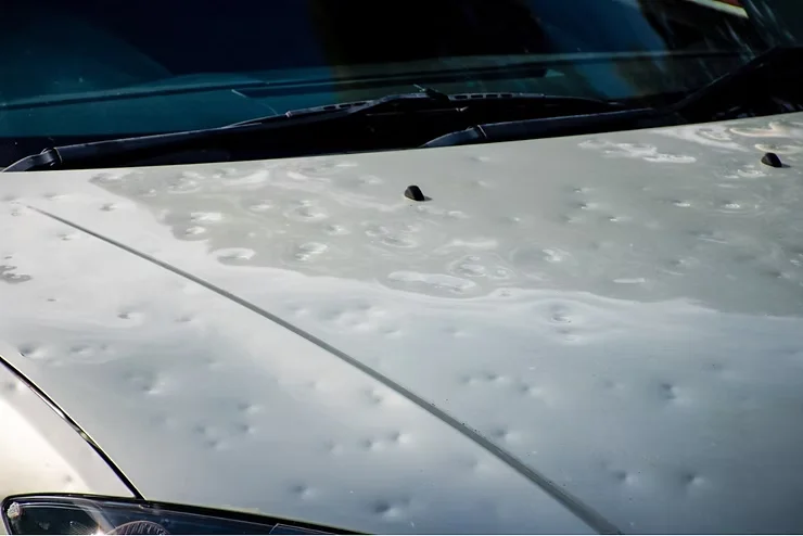 Car hood showing multiple dents caused by hail damage, illustrating the effects of harsh winter weather on unprotected vehicle paint.