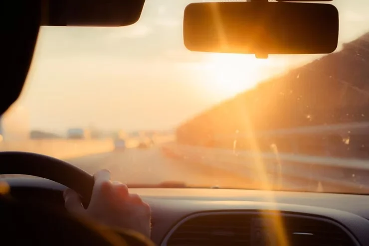 Driver’s hand on steering wheel with bright sunlight pouring through windshield, showing UV exposure inside car