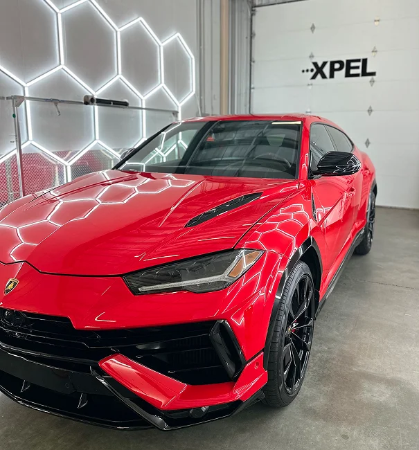 Red Lamborghini Urus with tinted windows reflecting LED lights inside XPEL-certified studio with installer applying film