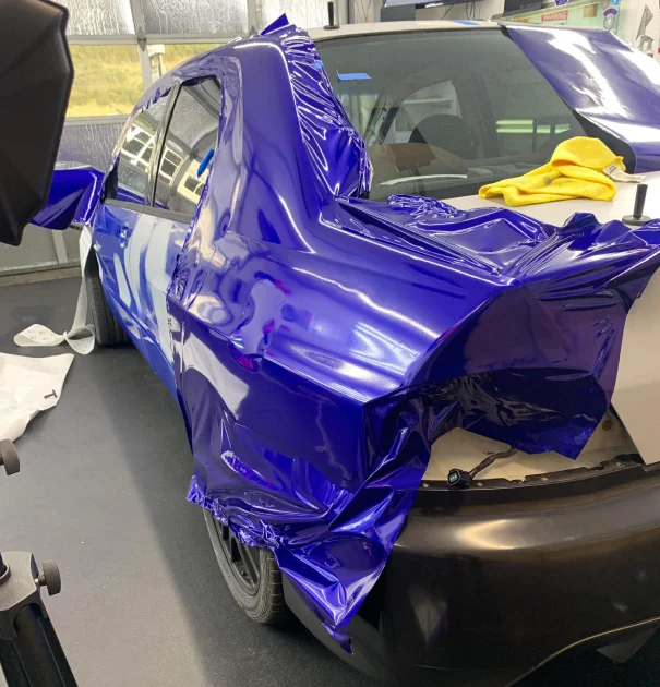 Close-up of a car in the process of receiving a vibrant blue vinyl wrap at an auto shop.
