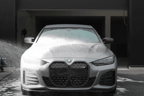 Detailing professional performing a high-pressure foam wash on a car's side window and door