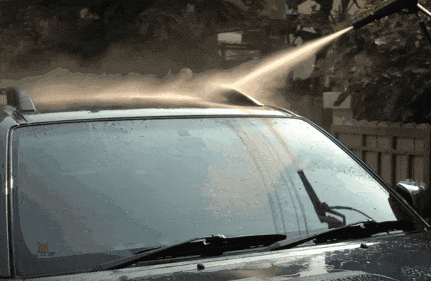 Close-up of a car windshield with water beading on the surface during a wash, highlighting hydrophobic coating effects.