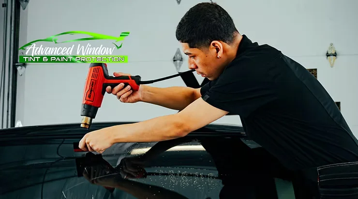 Technician applying window tint to a car using a heat gun at Advanced Window Tint & Paint Protection