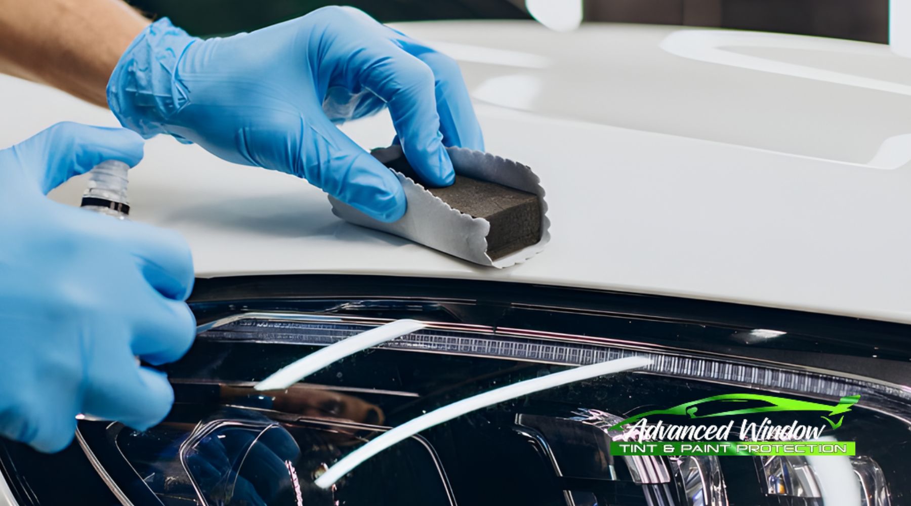 A professional wearing blue gloves applies ceramic coating to a white vehicle hood using a foam block wrapped in a microfiber cloth. The process takes place near the car’s headlight, emphasizing precision and care during application.