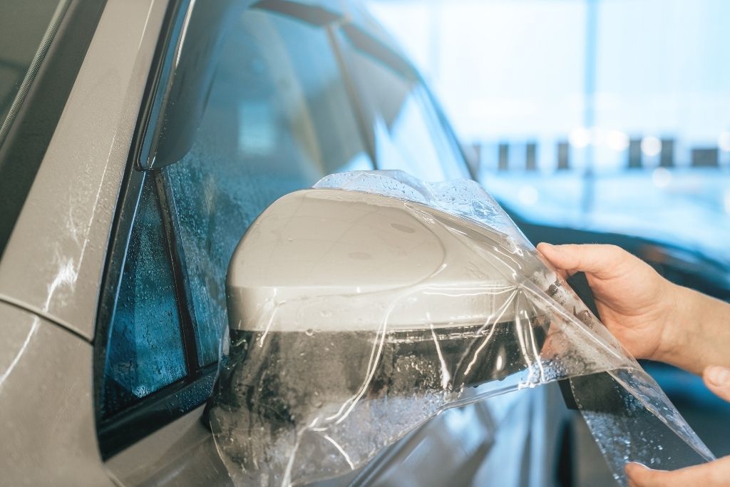 Technician applying paint protection film to a car side mirror during professional PPF installation.