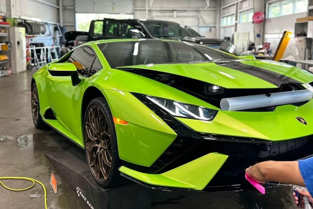 Bright green Lamborghini receiving detailing service in a professional auto shop, with a technician preparing the front bumper area.