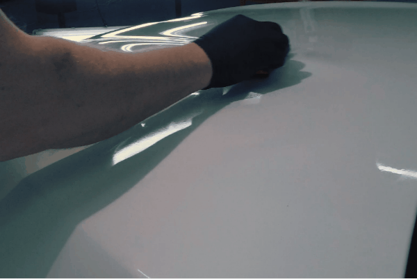 Technician applying ceramic coating to a white vehicle roof using a gloved hand for smooth, even coverage.