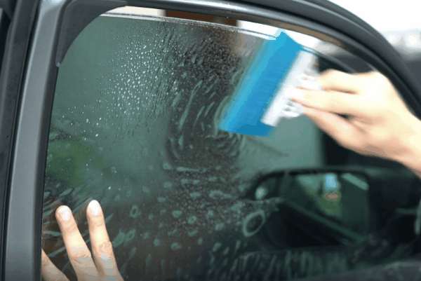Technician smoothing automotive window tint film onto car window using a squeegee during professional installation.
