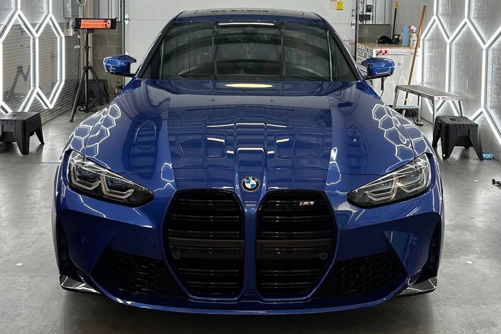 Front view of a blue BMW inside a professional automotive detailing and paint protection shop