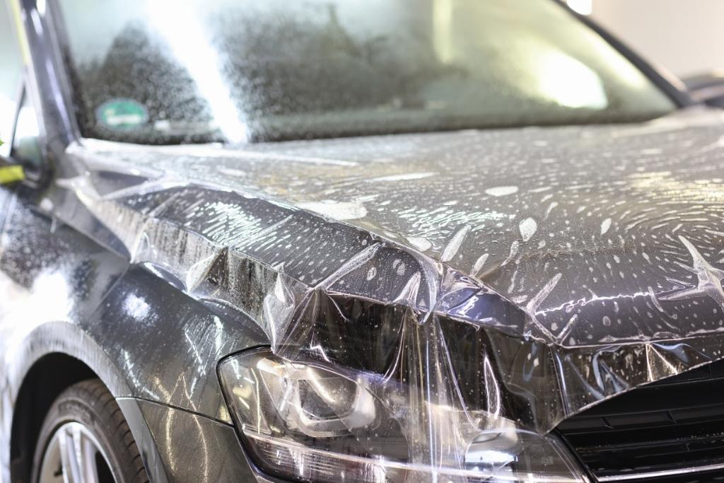 Clear paint protection film being applied to a car hood and headlight during professional PPF installation.