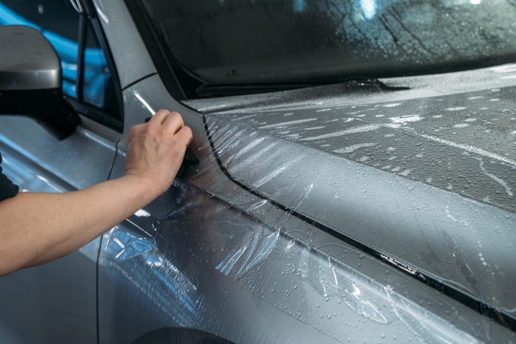 Technician applying paint protection film to the hood and fender of a vehicle to protect the paint from rock chips and road debris.