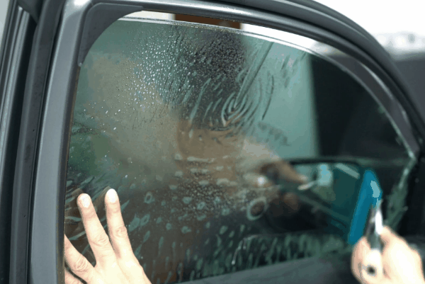 Close-up of a car window with old tint bubbling and hazy adhesive damage during window tint removal