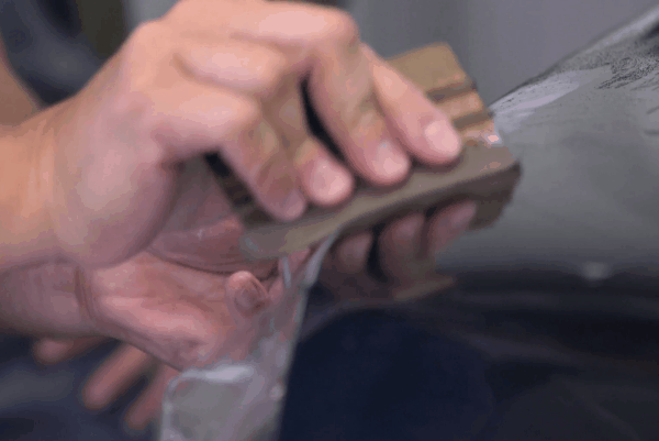 Technician applying clear paint protection film to a car panel during professional PPF installation.