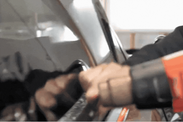 Technician using a heat gun to apply automotive window tint film on a vehicle window.