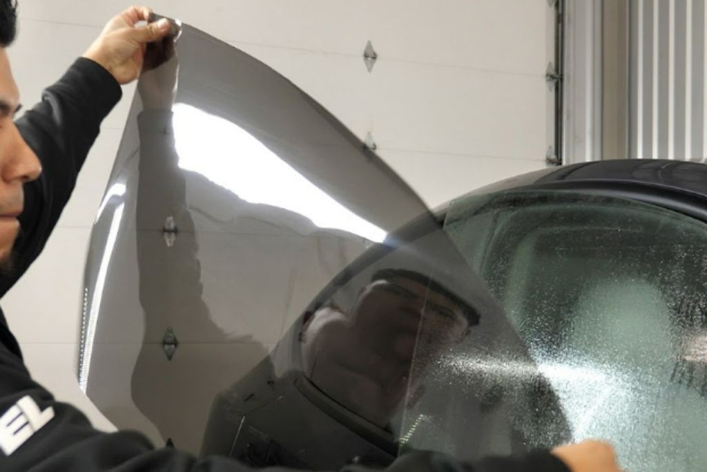 Installer applying window tint film to a vehicle window for heat rejection and UV protection.