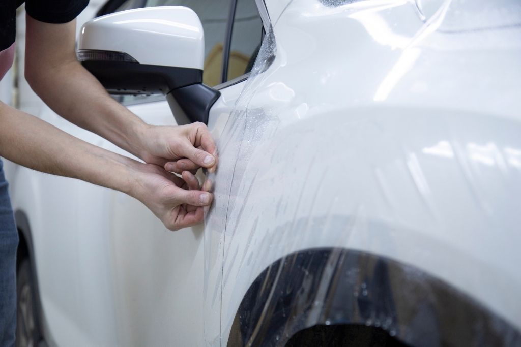 Technician applying clear paint protection film to the front fender of a white vehicle.