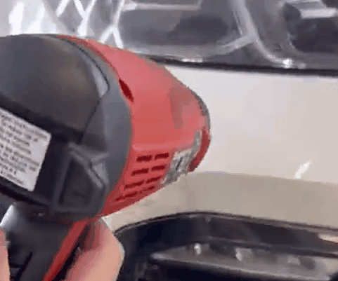 Technician using a heat gun to warm paint protection film on a vehicle panel during PPF removal.