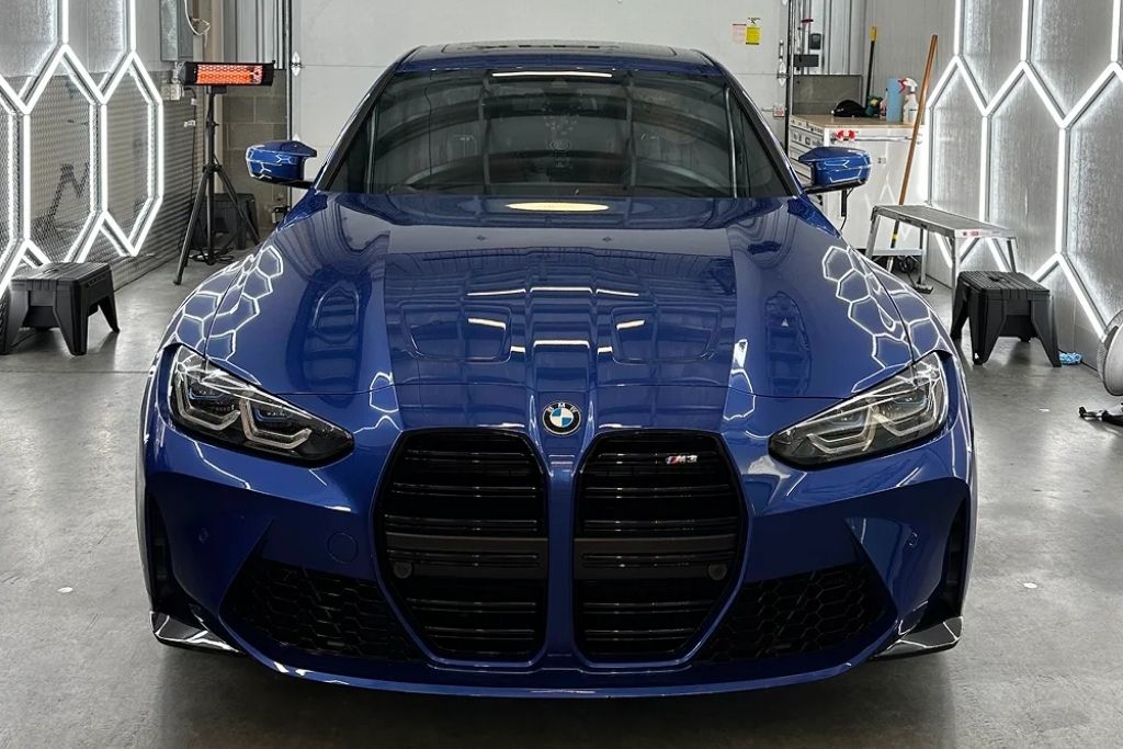 Blue BMW M4 inside a brightly lit PPF installation bay after paint protection film application.