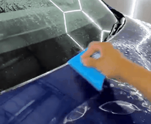 Installer uses a blue squeegee to apply paint protection film to the hood of a blue vehicle.