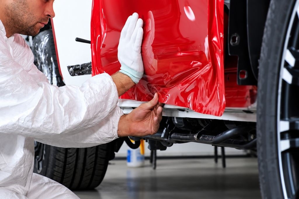 Professional installer applying red vinyl wrap to a vehicle body panel during a car wrap installation.