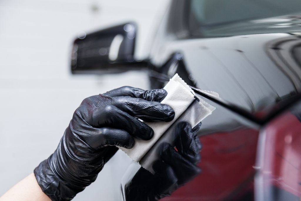 Technician wearing black gloves wiping a vehicle’s paint surface during ceramic coating preparation.