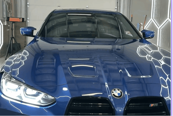 Blue BMW with a glossy, reflective paint finish inside the Advanced Window Tinting & PPF shop.
