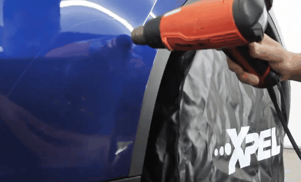 Heat gun warming self-healing PPF on a blue vehicle to help reduce the appearance of light surface scratches.